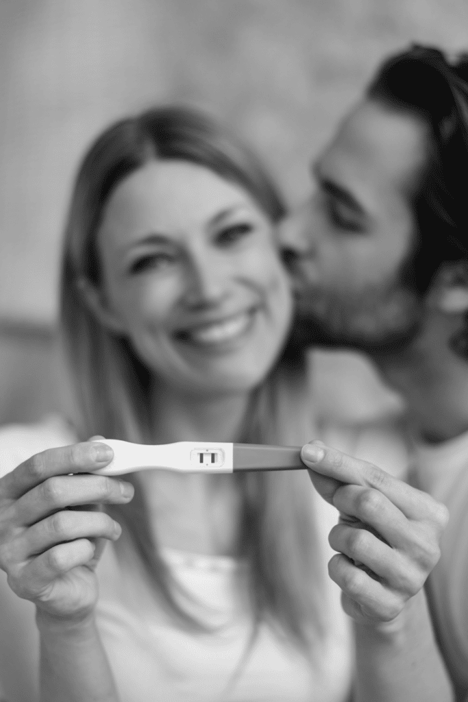 woman holding her pregnancy test with partner giving her a kiss, woman is smiling