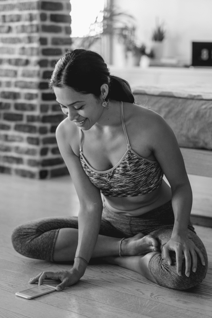 woman in yoga pose, looking at a workout app on smartphone